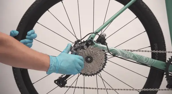 Maintenant, je vais démonter la roue arrière de ce vélo électrique. Les mains gantées tiennent la roue et le dérailleur.