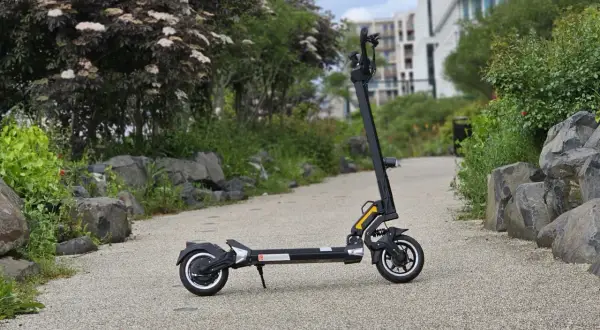 Trottinette électrique Dualtron Togo noire, sur un chemin pavé, avec des rochers et de la végétation.