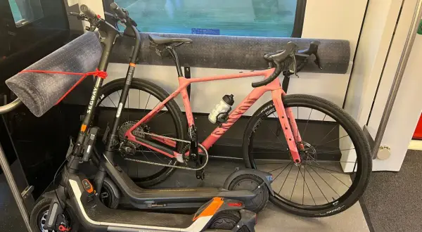 Une trottinette et un vélo rose sont rangés dans un compartiment de train, prêts pour l'aventure.