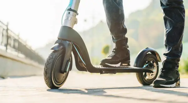 Pieds sur une trottinette électrique à vendre, prête pour une balade ensoleillée.
