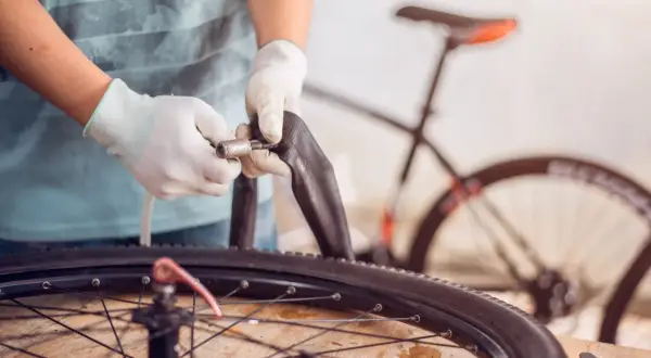 Mains gantées manipulant une chambre à air pour changer celle de la roue arrière d'un vélo électrique.