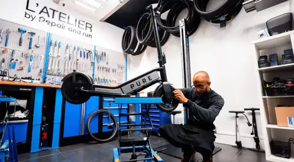 Un mécanicien ajuste une trottinette électrique PURE dans un atelier. Idéal pour ceux qui cherchent à vendre trottinette électrique ou à la faire réparer.