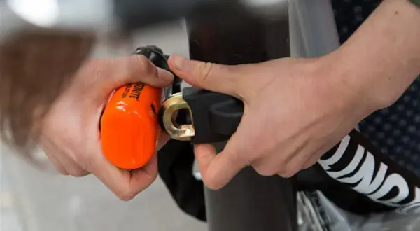 Mains sécurisant un vélo avec un antivol alarme orange vif. Le cadenas est solidement attaché au cadre.