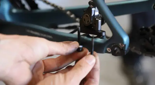 Mains ajustant la vis du frein à disque 140mm sur un cadre de vélo bleu.