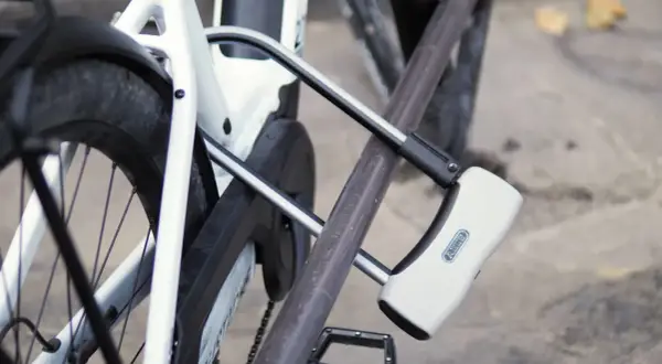 Un antivol pour vélo avec alarme intégrée protège un vélo blanc. Le cadenas en U est fixé au cadre et à la roue arrière.