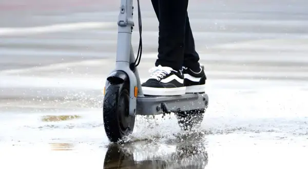 Trottinette électrique en action, éclaboussant l'eau sous la pluie. La protection ip54 assure une résistance à l'eau pour continuer le trajet.
