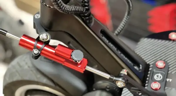 Amortisseur de direction trottinette rouge vif, fixé sur le châssis noir, prêt à améliorer la stabilité.