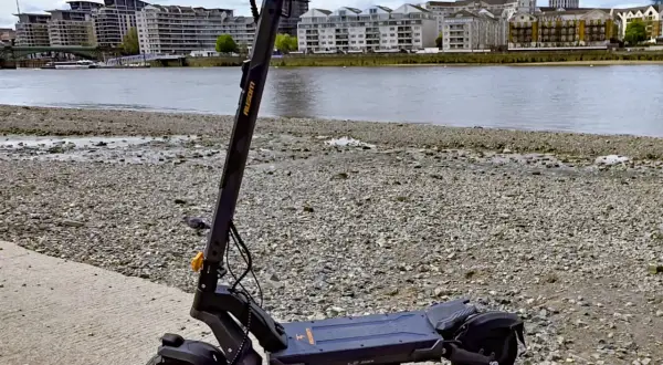 Trottinette électrique noire posée sur un chemin de gravier, avec une rivière et des immeubles en arrière-plan. Idéal pour savoir où garer sa trottinette électrique.