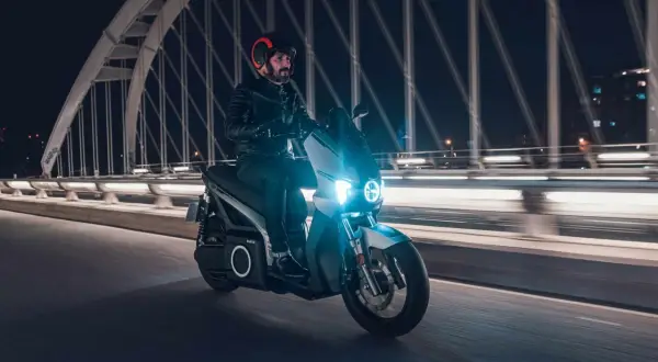 Un homme roule en scooter électrique sur un pont la nuit, profitant de la récupération d'énergie pour prolonger son trajet.