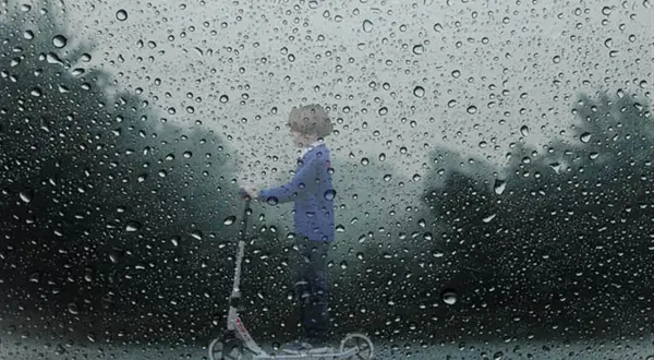 Un enfant sur une trottinette, sous la pluie. Le **signification IP54** protège de la poussière et des éclaboussures.