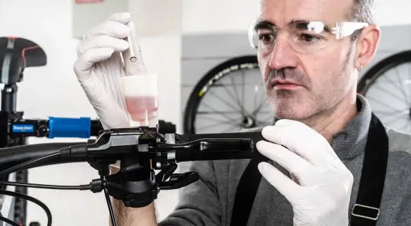 Un mécanicien effectue le purge frein a disque velo, ajoutant du liquide de frein avec une seringue.