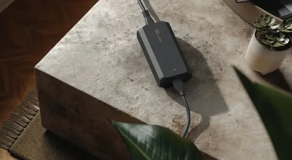 Chargeur 48v noir, compact et discret, posé sur une table en pierre. Une petite plante verte et des livres sont à proximité.