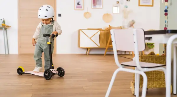 Un enfant porte un casque et se tient sur une trottinette rose. Il semble prêt à explorer, peut-être avec des stickers trottinette personnalisés pour ajouter une touche de couleur.