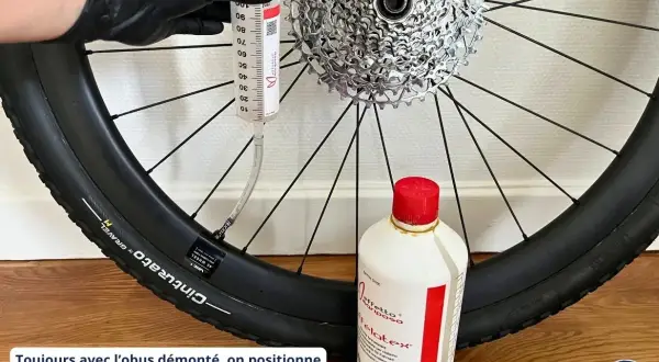 Maintenant, découvrez comment mettre liquide préventif tubeless : une seringue injecte le produit dans le pneu de vélo, à côté d'une bouteille de liquide.