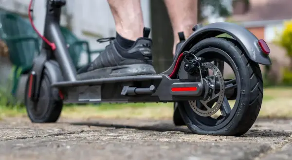 Pieds sur une trottinette électrique, le pneu arrière est visiblement crevé, rendant le trajet difficile.
