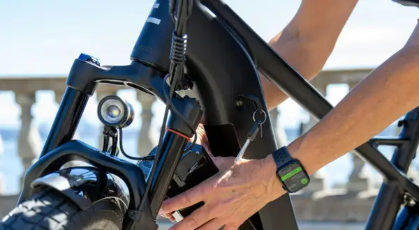 Main d'une personne âgée insérant la clé dans le cadre d'un vélo électrique. La montre connectée affiche "End Workout".