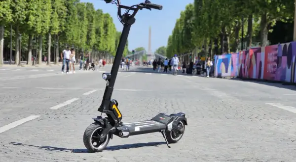 Trottinette électrique Dualtron Togo Plus sur une avenue bordée d'arbres, avec des passants et des décorations colorées en arrière-plan.
