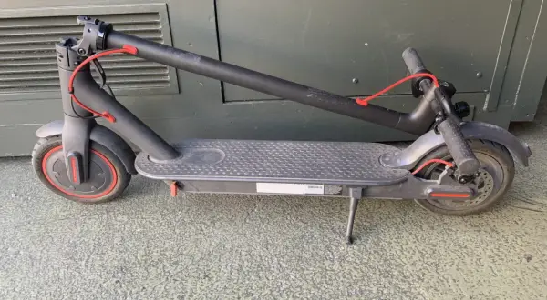 Trottinette électrique noire pliée, avec un câble rouge visible. Un kit d'étanchéité pour trottinette électrique pourrait être utile pour la protéger.