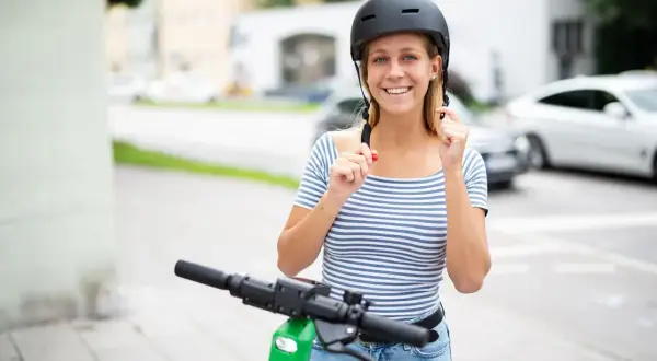 Jeune femme souriante ajustant son casque trottinette électrique, prête pour une balade en ville.