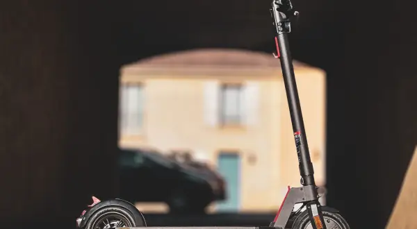 Trottinette électrique Wispeed T850 noire, vue de profil, devant une maison floue.