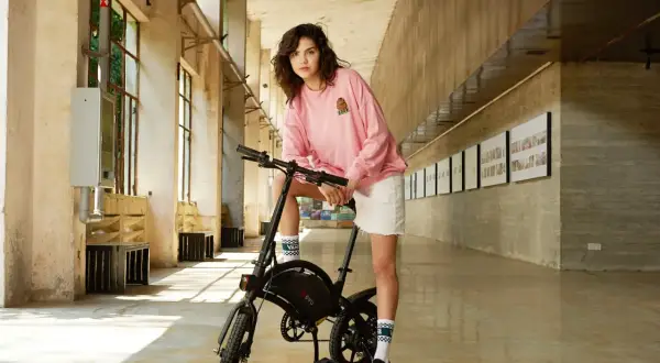Jeune femme posant avec un vélo électrique DYU dans un couloir moderne.