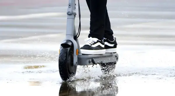 Une trottinette électrique roule dans une flaque d'eau, soulevant des éclaboussures. La question est : peut-on rouler sous la pluie avec une trottinette électrique ?