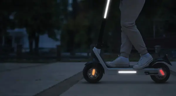 Une trottinette électrique avec une bande réfléchissante sur le guidon et le plateau, pour une visibilité accrue la nuit.