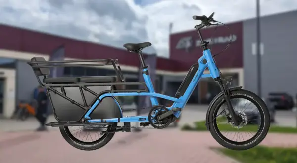 Vélo longtail bleu électrique, idéal pour transporter des passagers ou des courses grâce à sa longue plateforme arrière et ses sièges.