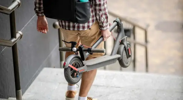 Un homme porte sa trottinette électrique pliée, peut-être pour la vendre ou la transporter.
