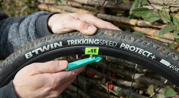 Main d'un cycliste ajustant une chambre à air 700x40c sur une roue de vélo, avec un démonte-pneu vert.