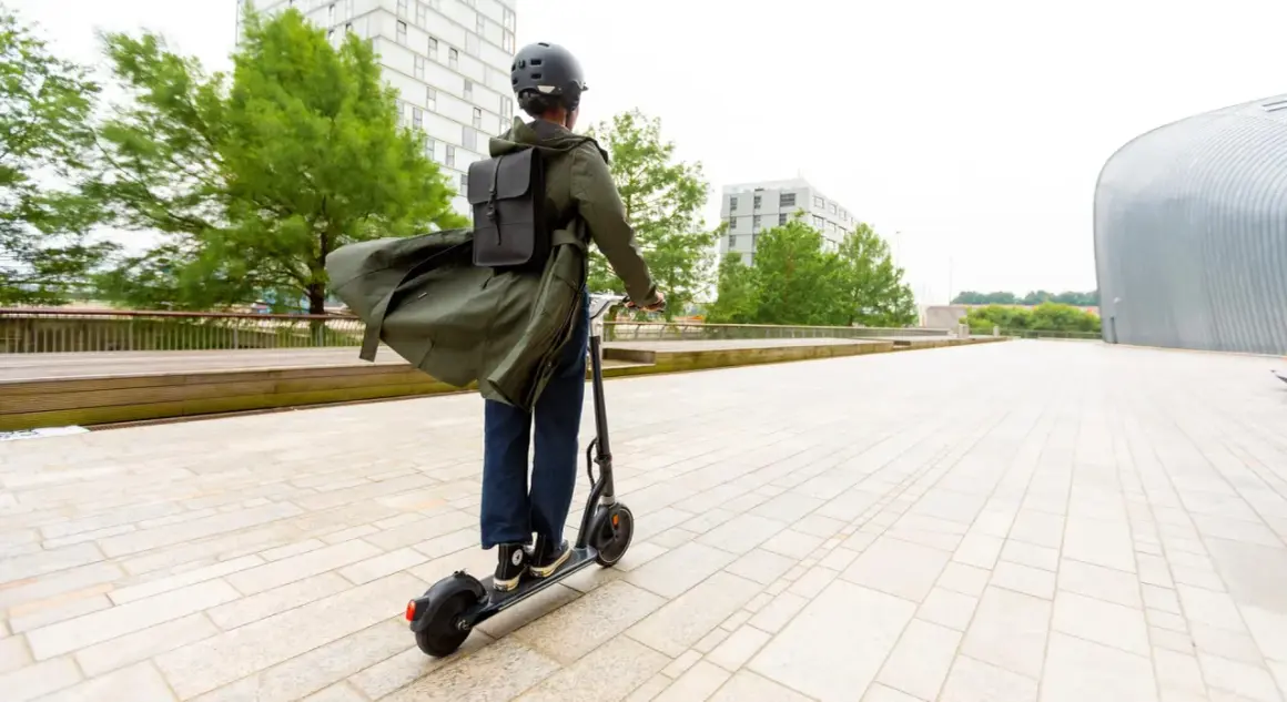 Personne casquée sur trottinette électrique, manteau long flottant, pour augmenter l'autonomie de sa trottinette électrique en ville.