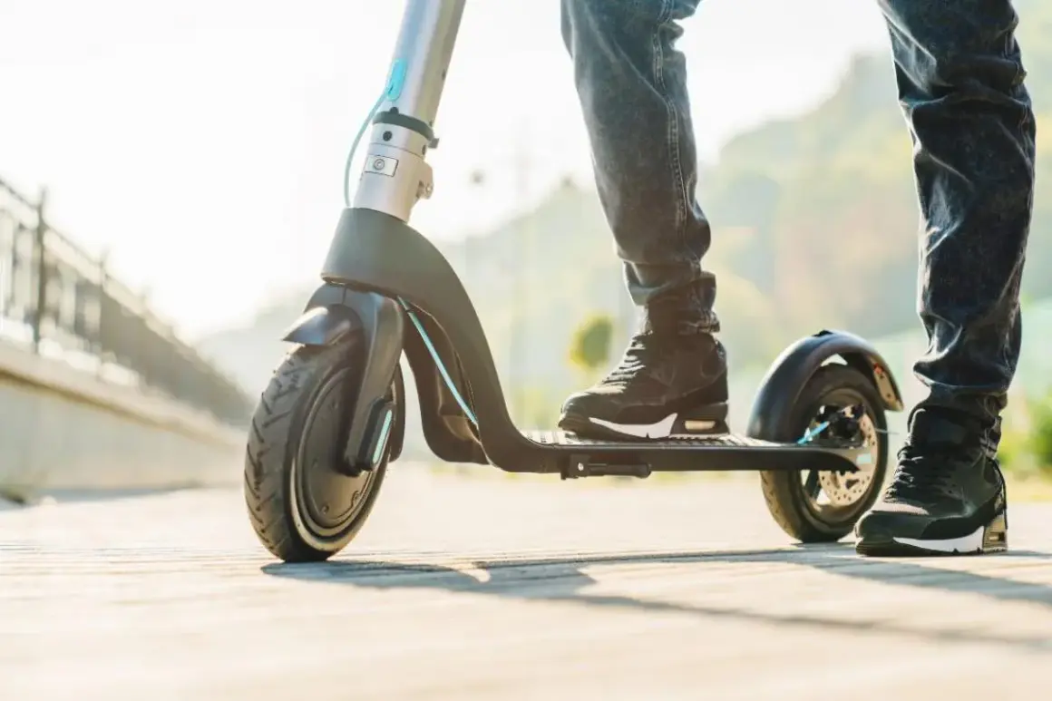 Pieds sur une trottinette électrique à vendre, prête pour une balade ensoleillée.