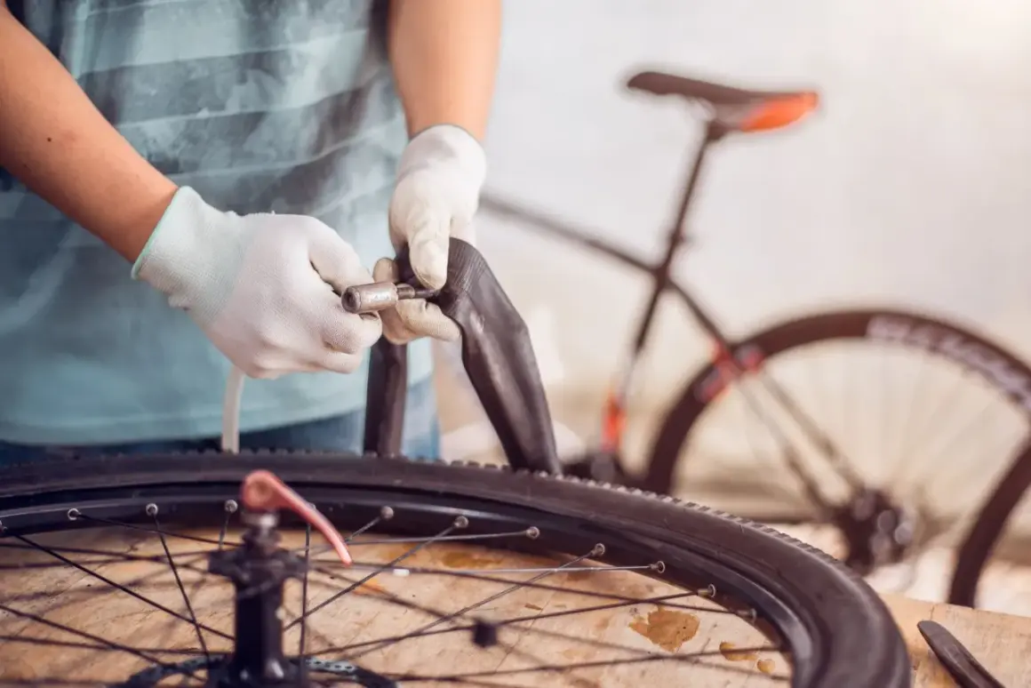 Mains gantées manipulant une chambre à air pour changer celle de la roue arrière d'un vélo électrique.