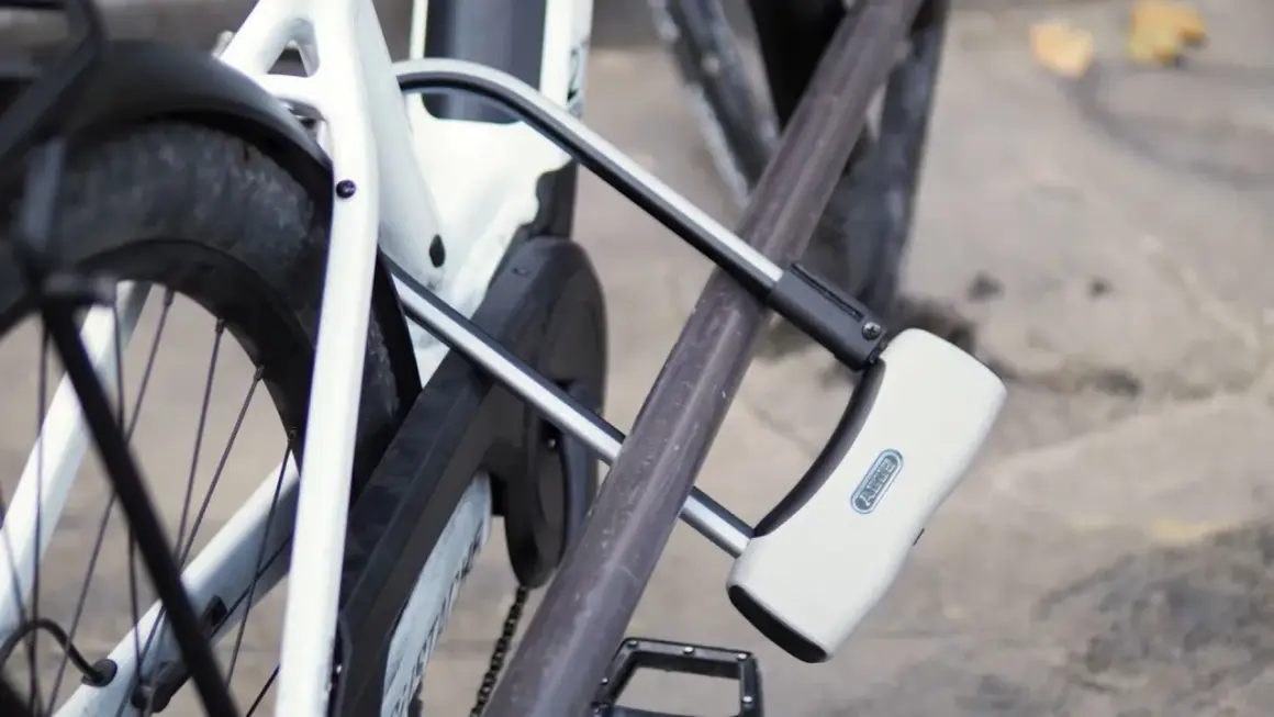 Un antivol pour vélo avec alarme intégrée protège un vélo blanc. Le cadenas en U est fixé au cadre et à la roue arrière.