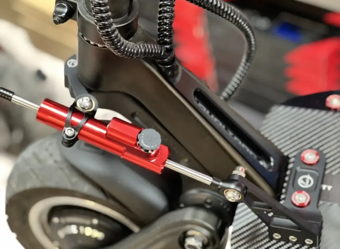 Amortisseur de direction trottinette rouge vif, fixé sur le châssis noir, prêt à améliorer la stabilité.