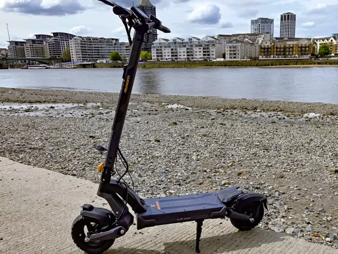 Trottinette électrique noire posée sur un chemin de gravier, avec une rivière et des immeubles en arrière-plan. Idéal pour savoir où garer sa trottinette électrique.