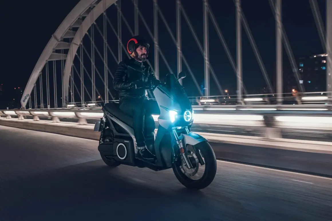 Un homme roule en scooter électrique sur un pont la nuit, profitant de la récupération d'énergie pour prolonger son trajet.