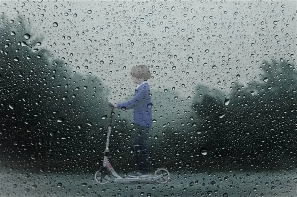 Un enfant sur une trottinette, sous la pluie. Le **signification IP54** protège de la poussière et des éclaboussures.
