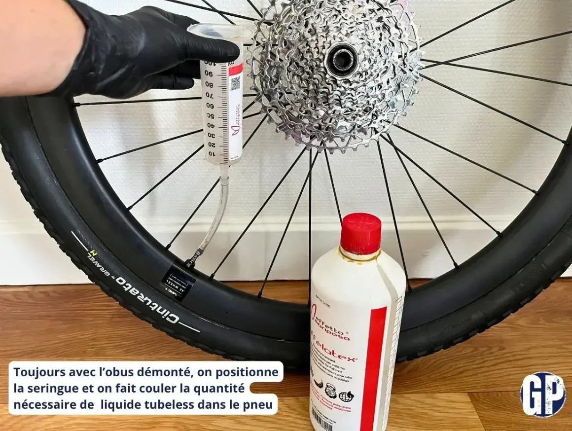 Maintenant, découvrez comment mettre liquide préventif tubeless : une seringue injecte le produit dans le pneu de vélo, à côté d'une bouteille de liquide.