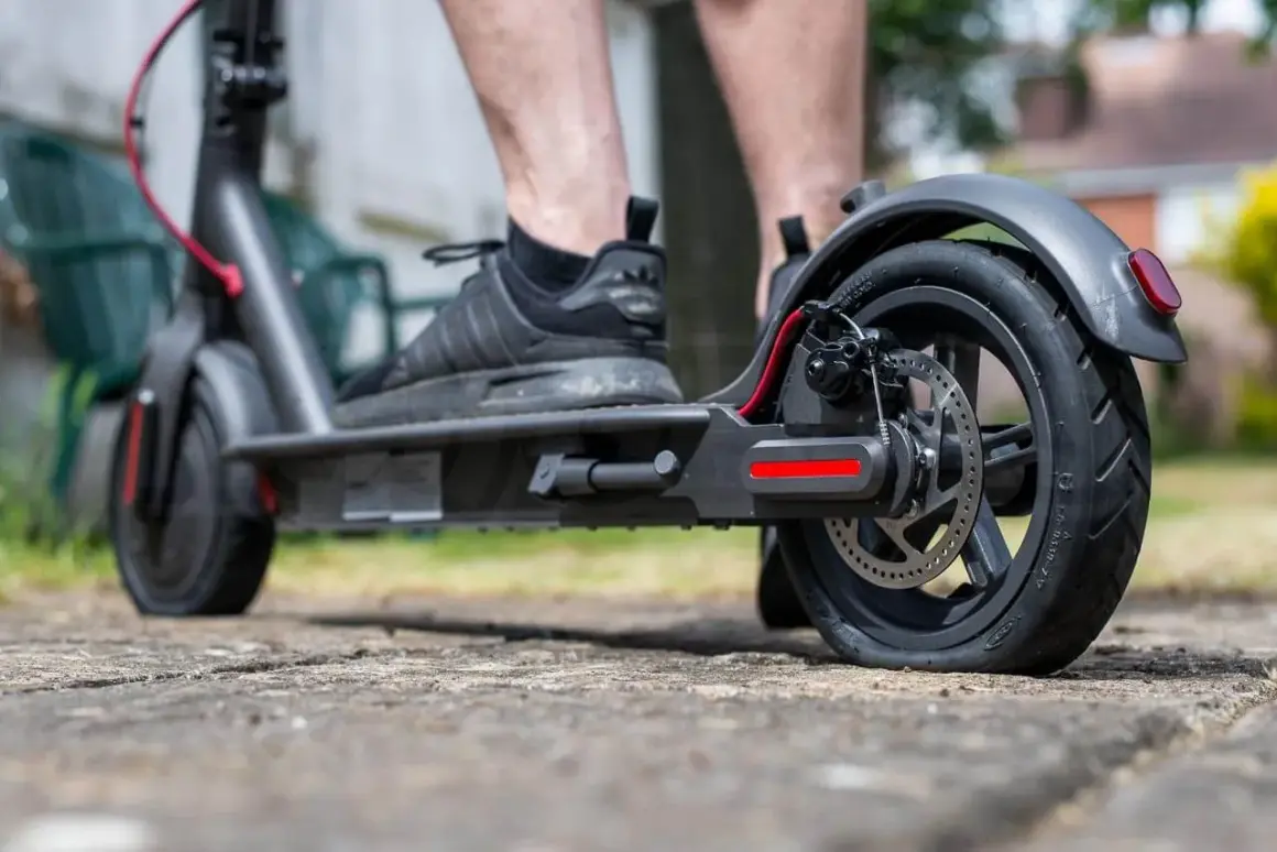 Pieds sur une trottinette électrique, le pneu arrière est visiblement crevé, rendant le trajet difficile.
