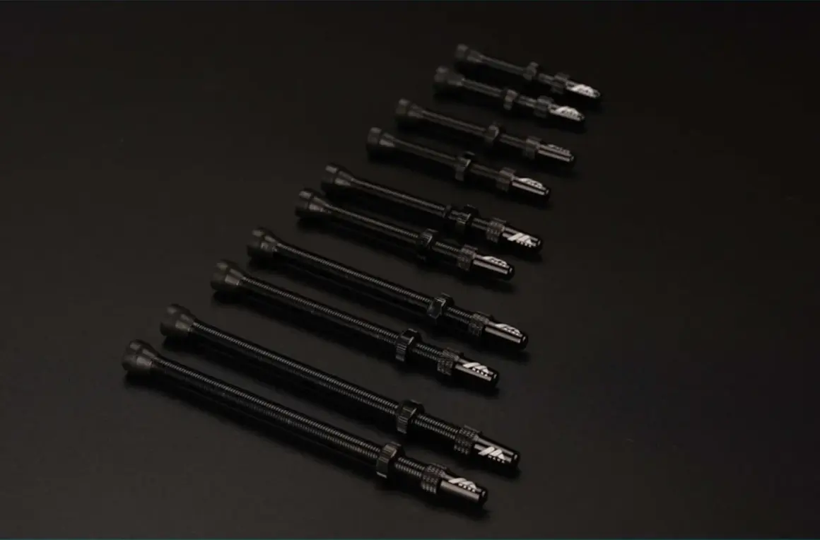 Plusieurs valves Schrader noires, alignées sur un fond sombre, prêtes pour une nouvelle aventure cycliste.