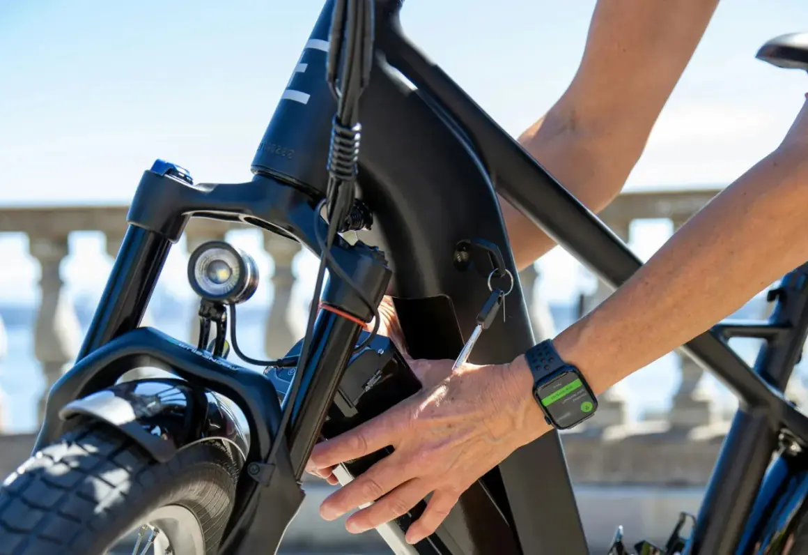 Main d'une personne âgée insérant la clé dans le cadre d'un vélo électrique. La montre connectée affiche "End Workout".