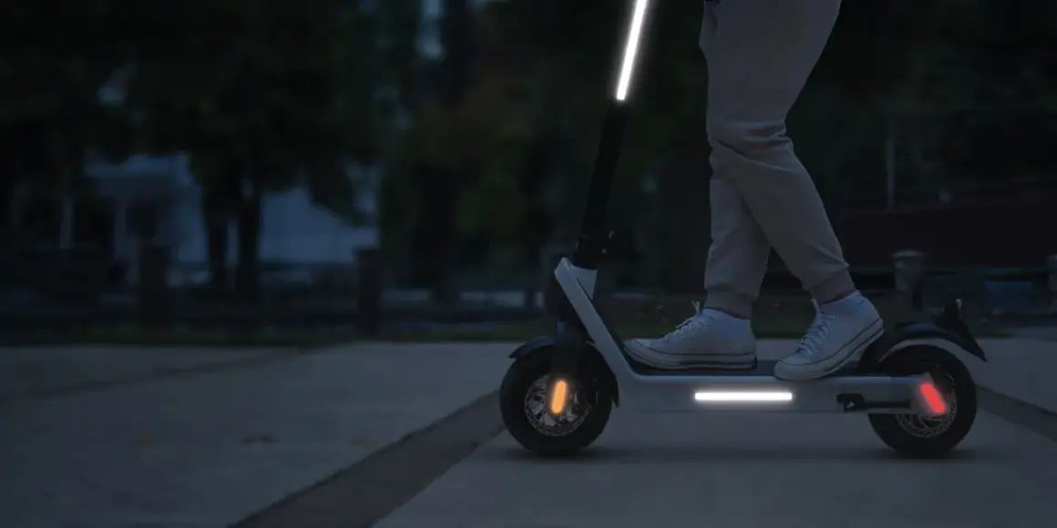 Une trottinette électrique avec une bande réfléchissante sur le guidon et le plateau, pour une visibilité accrue la nuit.