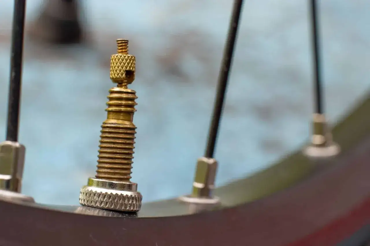 Gros plan sur une valve de pneu de v&eacute;lo, type presta ou schrader, en laiton, avec des rayons en arri&egrave;re-plan.