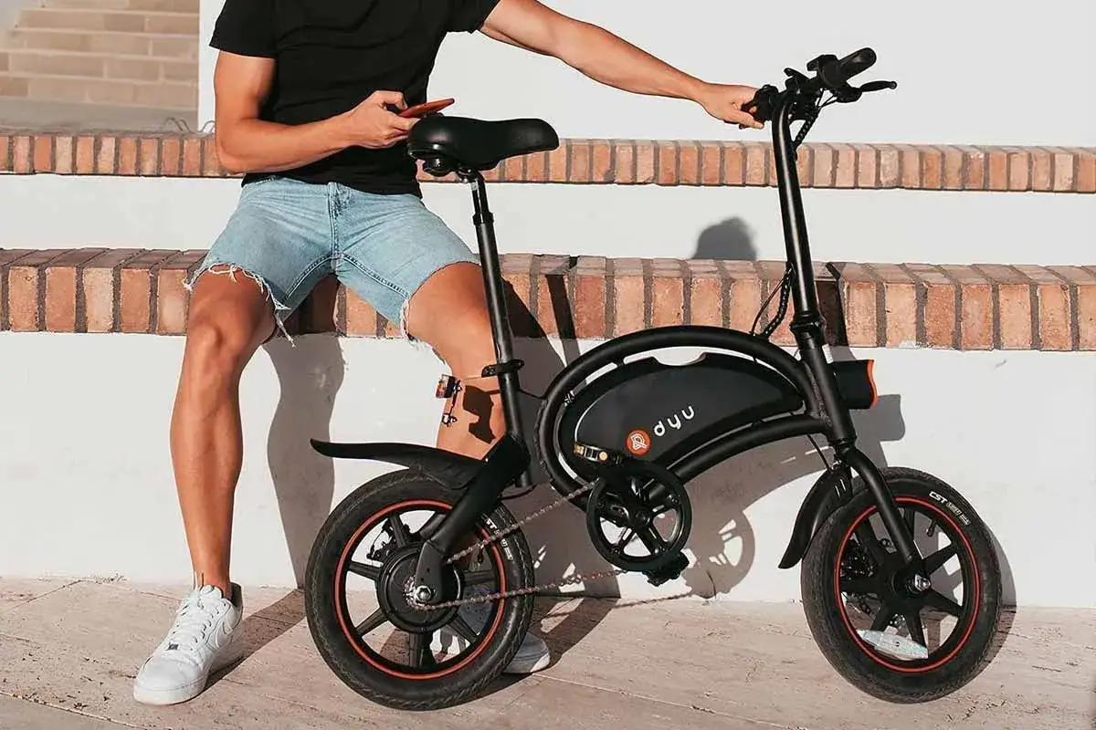 Un homme en short regarde son téléphone, assis à côté d'un vélo électrique noir dyu d3.