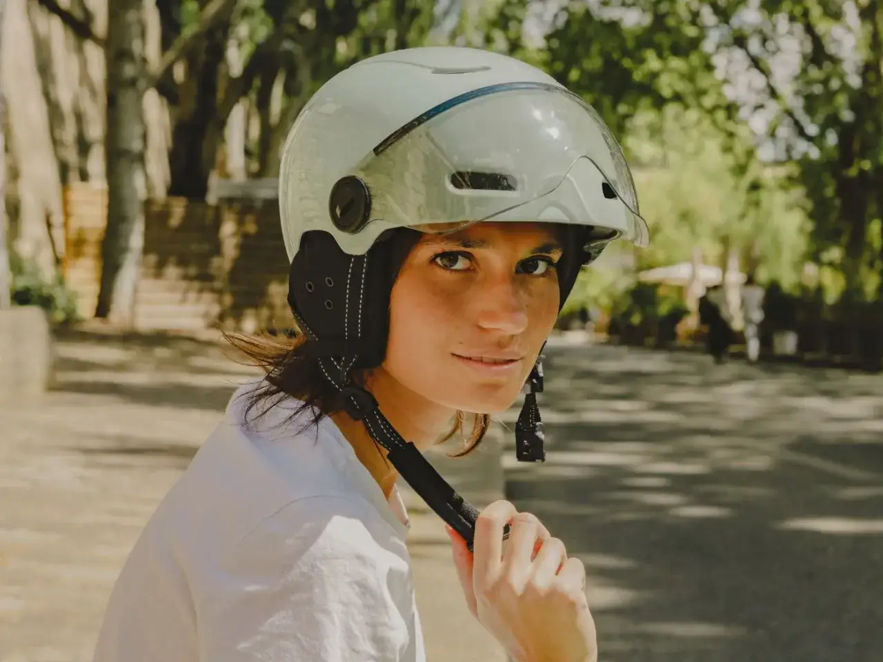 Jeune femme souriante portant un casque trottinette &eacute;lectrique, pr&ecirc;te pour une balade ensoleill&eacute;e.