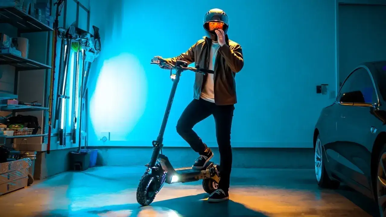 Un homme casqu&eacute; pose avec son trottinette &eacute;lectrique Dualtron origine, dans un garage &eacute;clair&eacute; par des n&eacute;ons bleus.