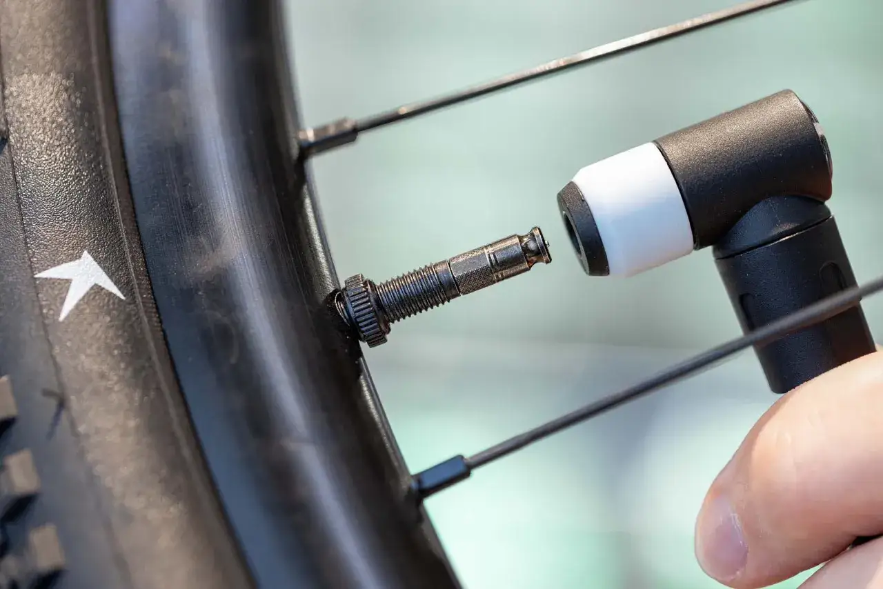 Une main connecte une pompe à un valve Schrader sur une roue de vélo.