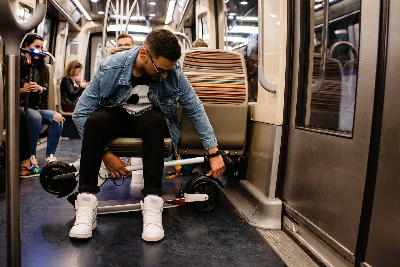 Un homme ajuste sa trottinette dans le train, prêt à poursuivre son trajet.