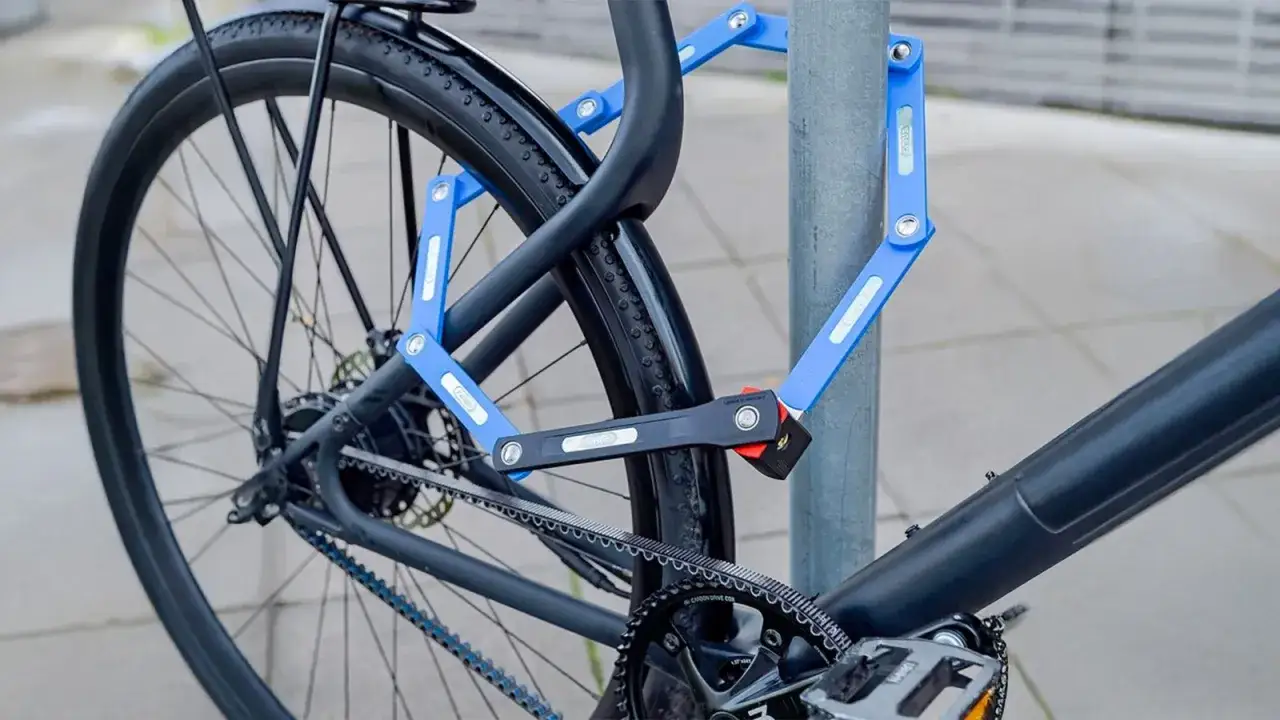 Vélo électrique sécurisé avec un antivol bleu pliable attaché à un poteau. Le cadenas protège le cadre et la roue arrière.
